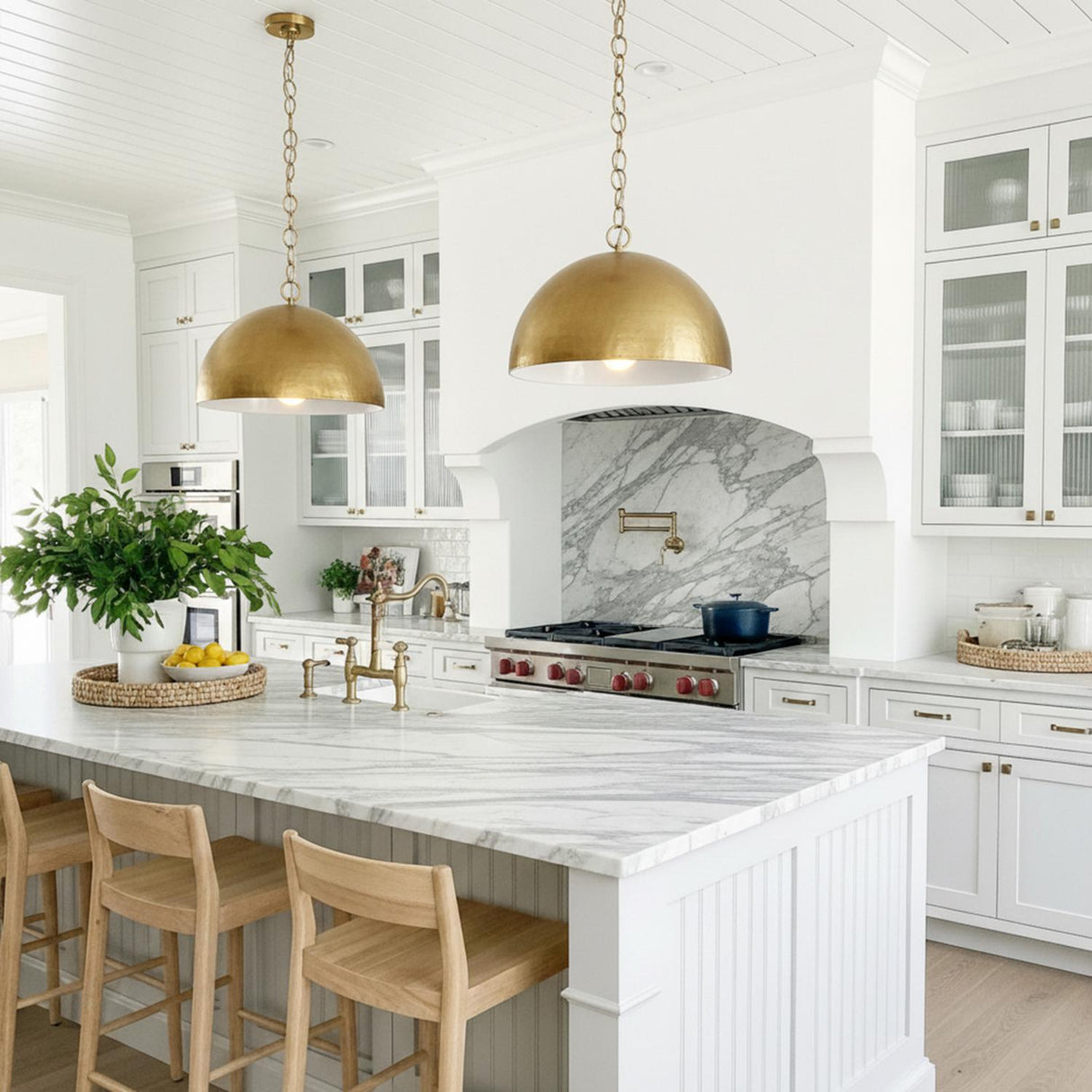 A farmhouse kitchen features two Arlen Pendant 24", Modern Brass pendants in a hammered brass finish over a white marble island under a white shiplap ceiling.
