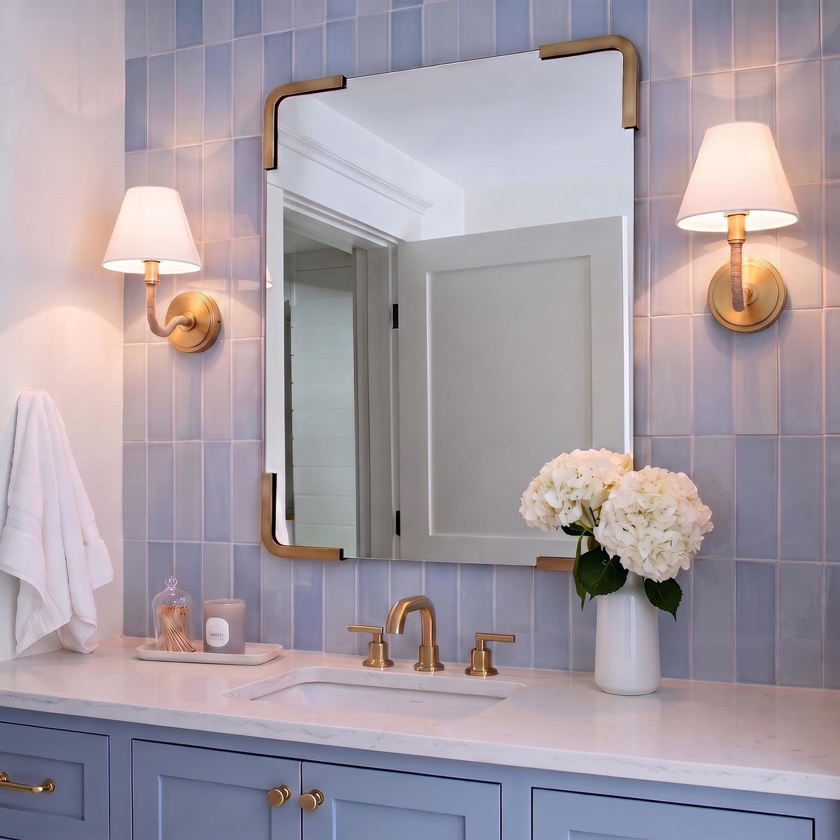 A transitional bathroom vanity features two Harlow Wall Sconce 9", Modern Brass with Rattan lights flanking a brass mirror over blue vertical subway tile.