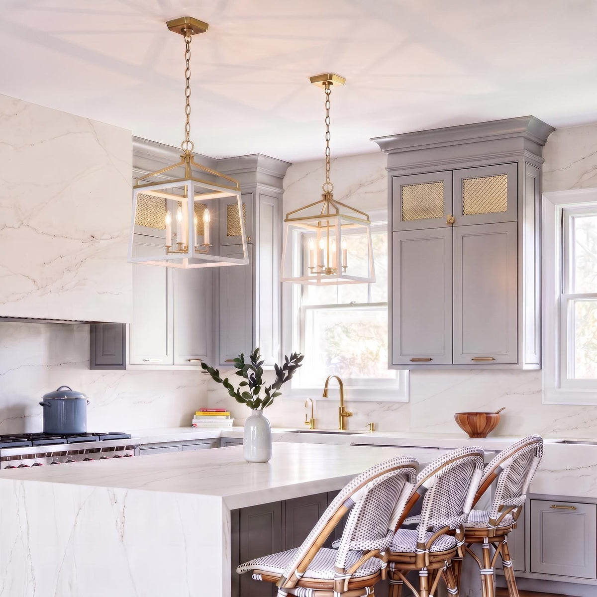 A transitional kitchen with two Fillmore Large Lantern Pendants in matte white and modern brass over a white marble waterfall island and gray shaker cabinets.