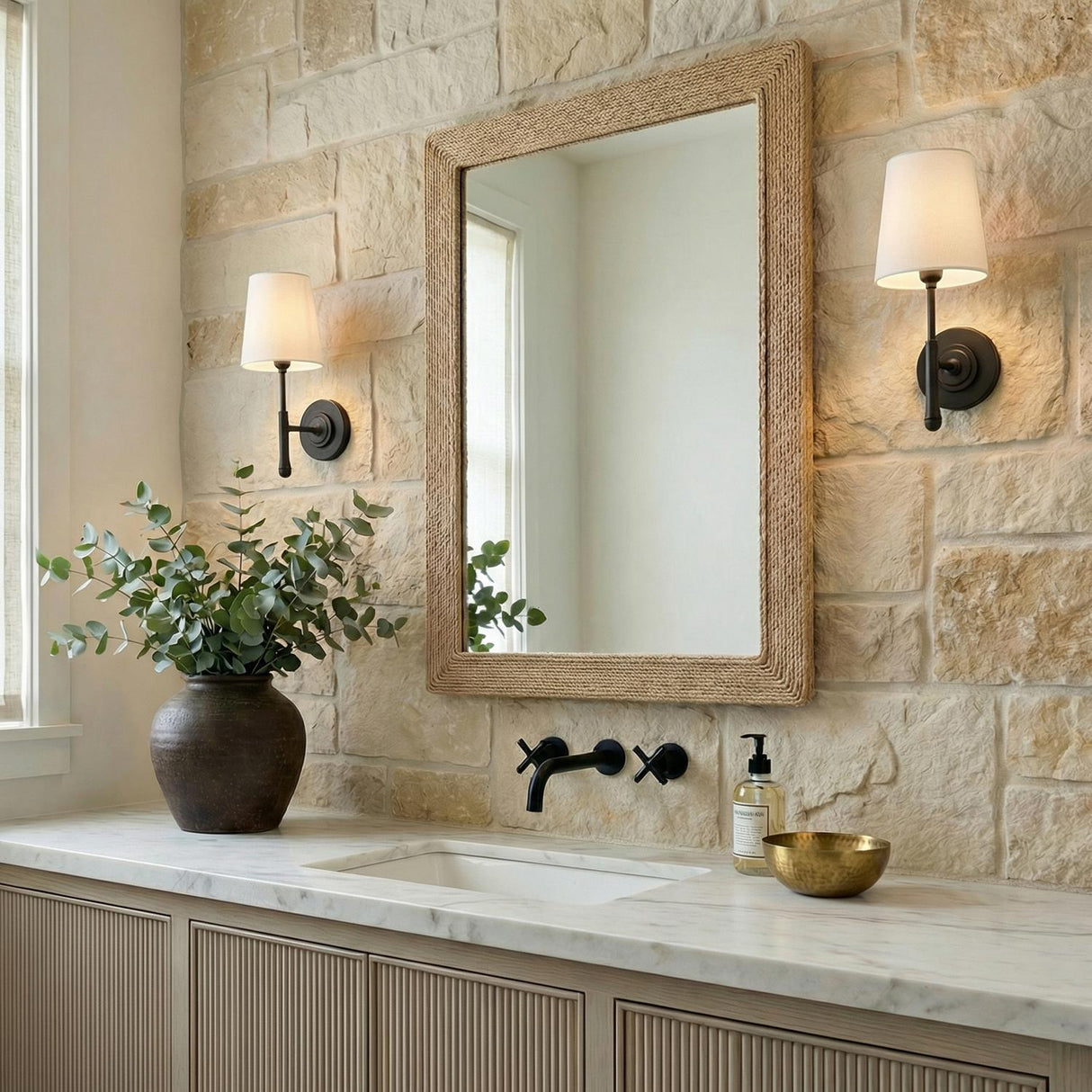 Emerson Wall Sconce 14", Aged Iron linear Wall Sconce in a Modern Farmhouse Bathroom with a stone wall and jute mirror.