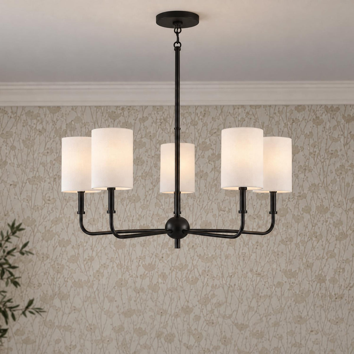 A transitional dining room features the Remington 5 Light Chandelier 26", Matte Black with white fabric shades suspended against floral wallpaper and crown molding.