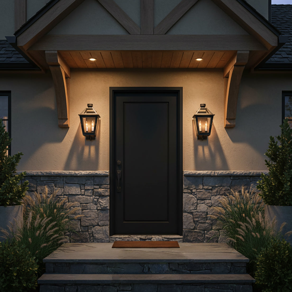 Fairmont Small Outdoor Wall Light 16, Textured Black - Two black lanterns with warm lighting flank a black front door with stone and stucco siding.