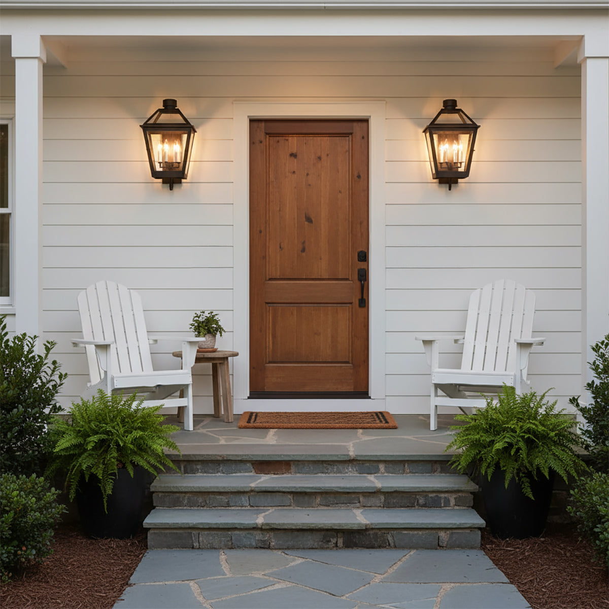 Fairmont Large Outdoor Wall Light 24 - Two black lanterns flanking a natural wood door on a white exterior with Adirondack chairs and potted ferns.