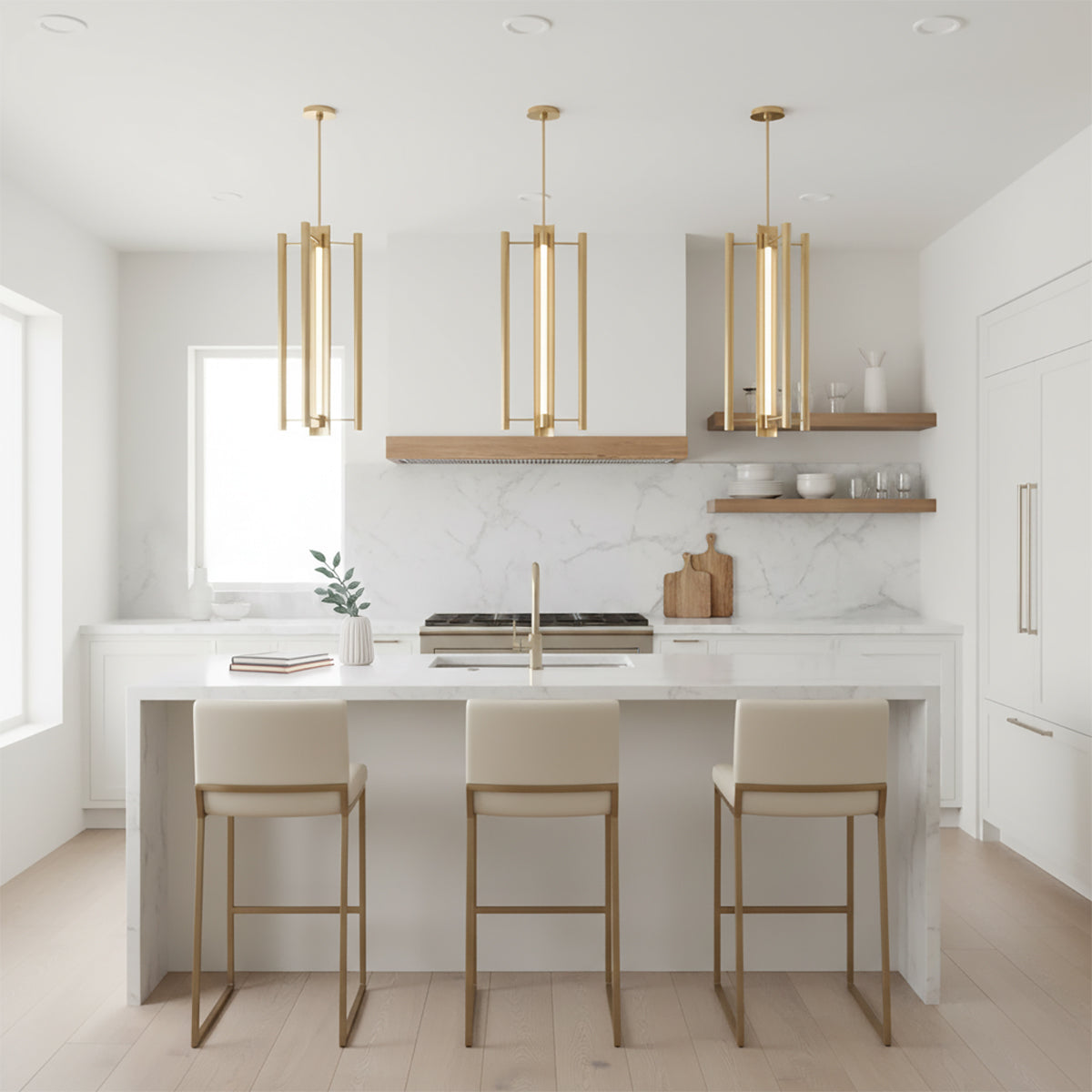 Robin Elongated 4 Light LED Pendant 16" Modern Brass - Three brass pendant lights hang above a kitchen island with bar stools, a marble backsplash, and a wooden range hood.