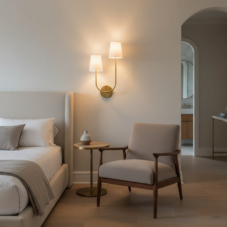 Greta Double Wall Sconce, Satin Brass - A satin brass double wall sconce illuminates a bedroom with a bed, chair, and side table.