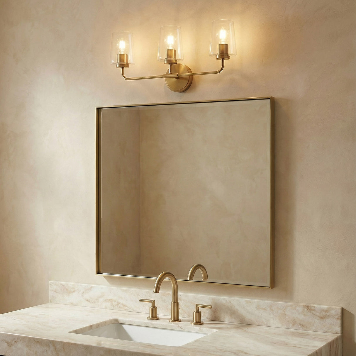 Wyatt 3 Light Vanity, Legacy Brass with Clear Glass geometric vanity in a Transitional Bathroom with a marble counter and gold faucet.