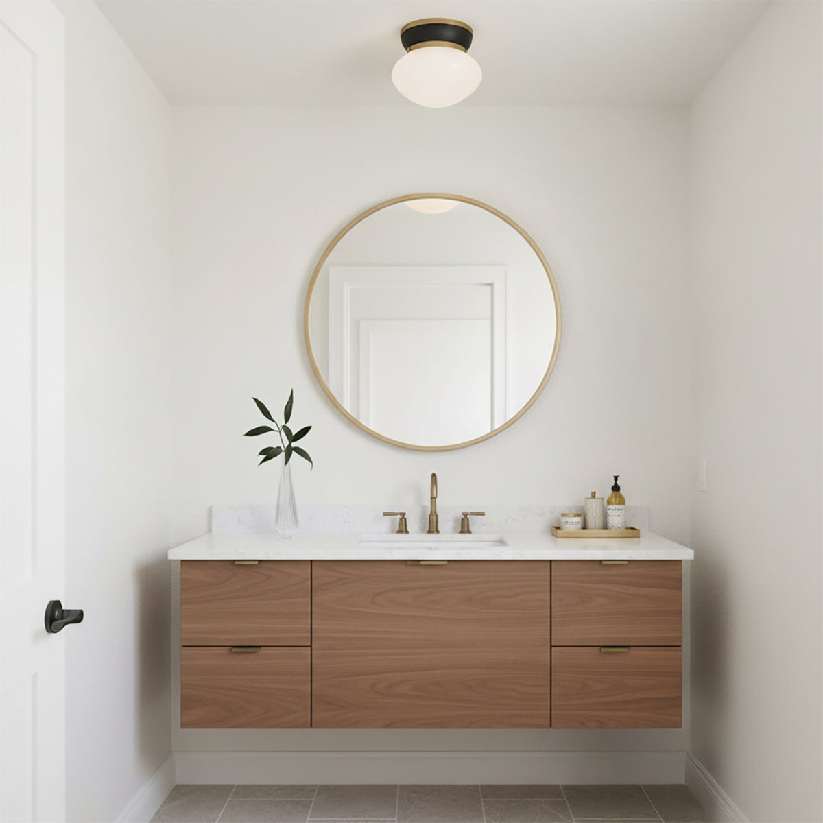 Piper Flush Mount 12, Satin Brass and Black - A flush mount light fixture with a black base and frosted glass shade is mounted on a white ceiling above a round gold mirror and a floating wood vanity in a bathroom.