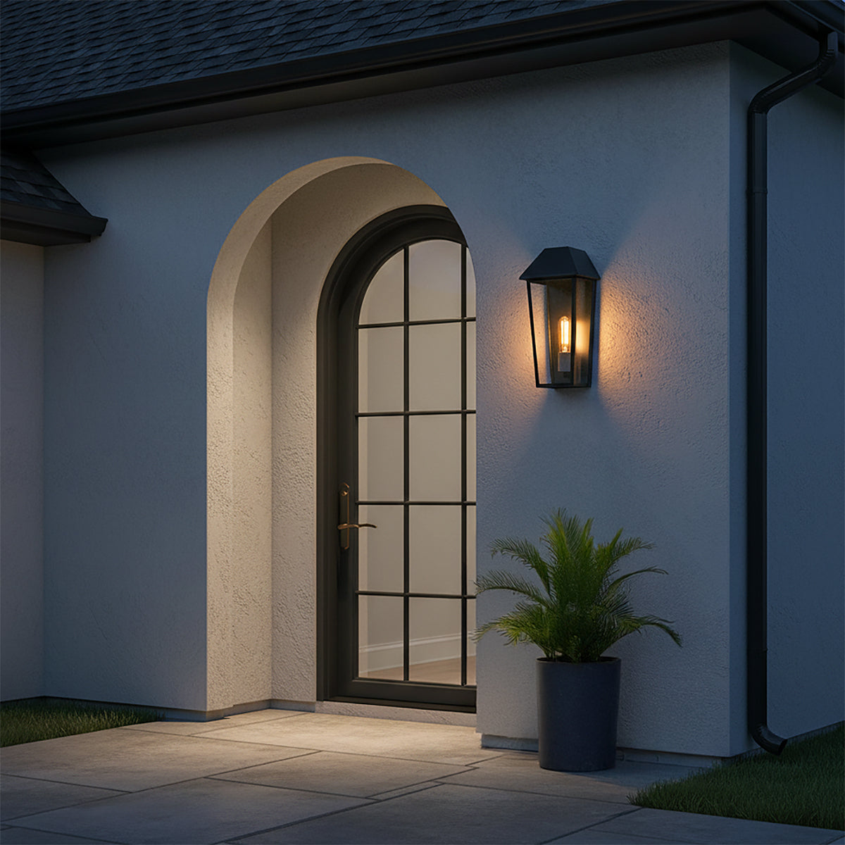 Lorimor Outdoor Wall Light, Medium 15" Black - Black lantern-style wall light illuminates a stucco entryway with an arched door and a potted plant.