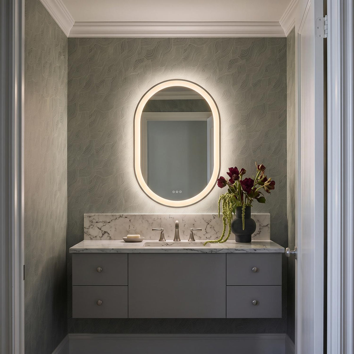 A transitional bathroom with the Sherman Medium LED Oval Mirror 24" x 36", Brushed Nickel mounted over a marble countertop and gray floating vanity with wave wallpaper.