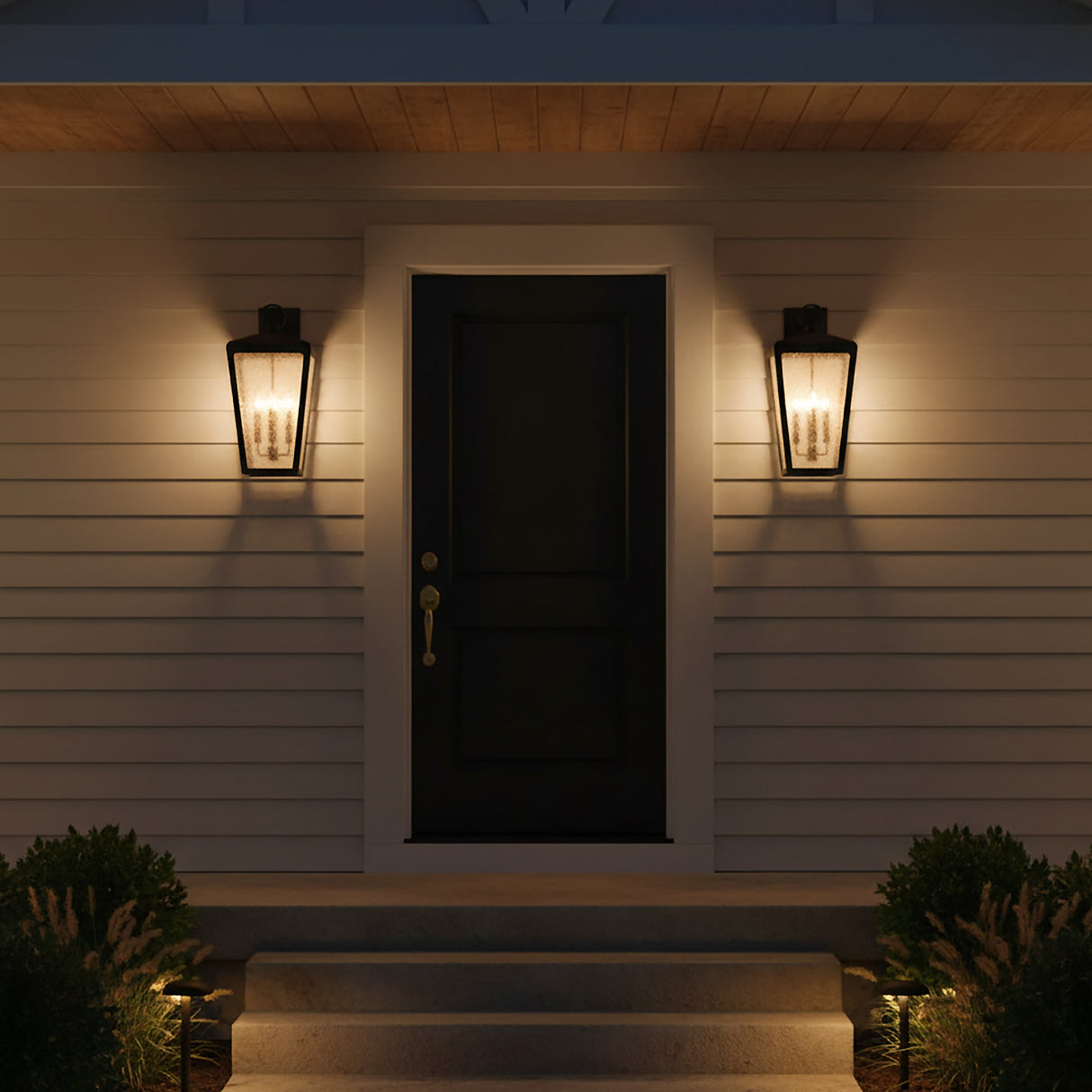 Barrett Outdoor Wall Light, Large 26" Textured Black - Two black lanterns on either side of a dark front door with light illuminating the porch steps and surrounding greenery.