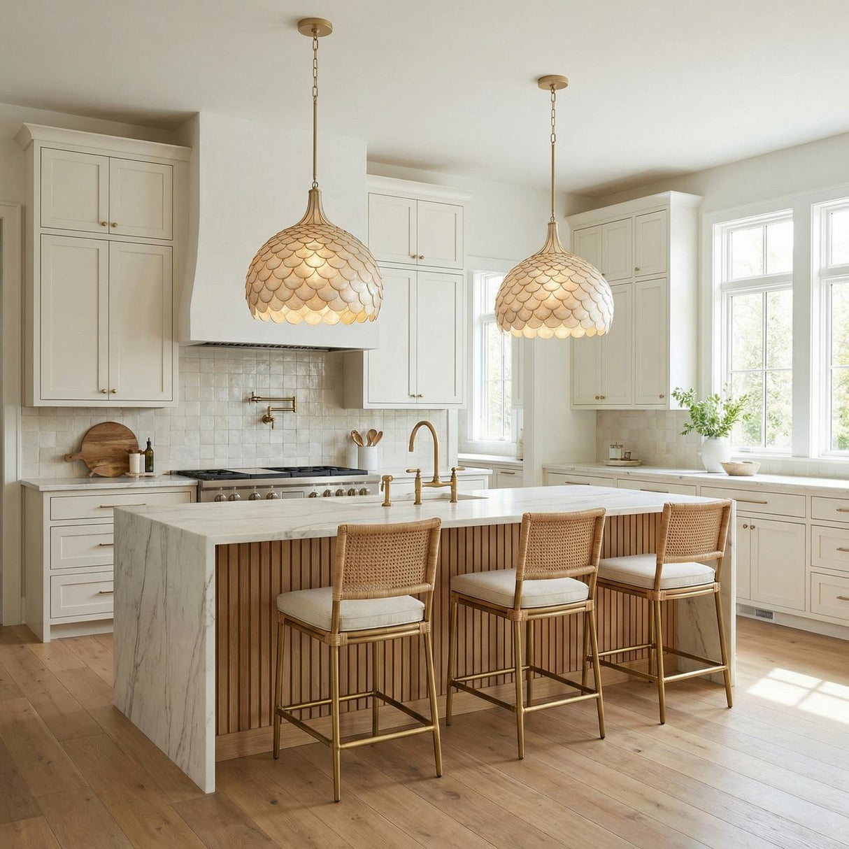 A coastal kitchen features two Valentina Large Pendant 21-inch Soft Brass and Capiz Shell pendants over a white marble waterfall island and white shaker cabinets.