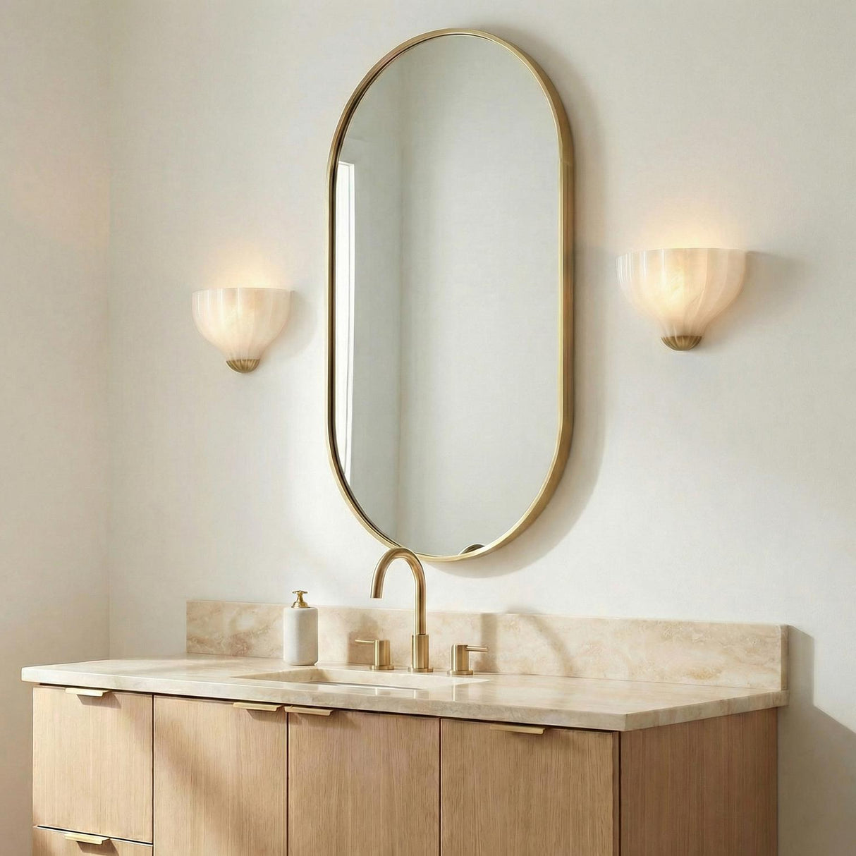 Claire Wall Sconce 9", Brass and Strie Glass scalloped Wall Sconce in a Contemporary Bathroom with an oval gold mirror and marble vanity.