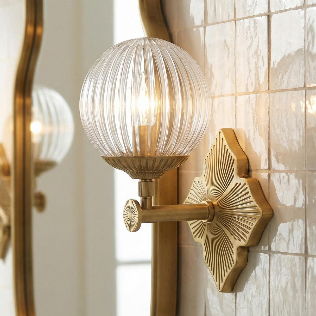 Victoria Wall Sconce, Aged Brass and Clear Ribbed Glass globe wall sconce in a Transitional Bathroom with zellige tiles and a wavy mirror.