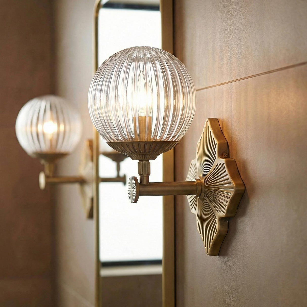 Victoria Wall Sconce 12", Aged Brass and Clear Ribbed Glass globe Wall Sconce in a Transitional Bathroom with a brass framed mirror.