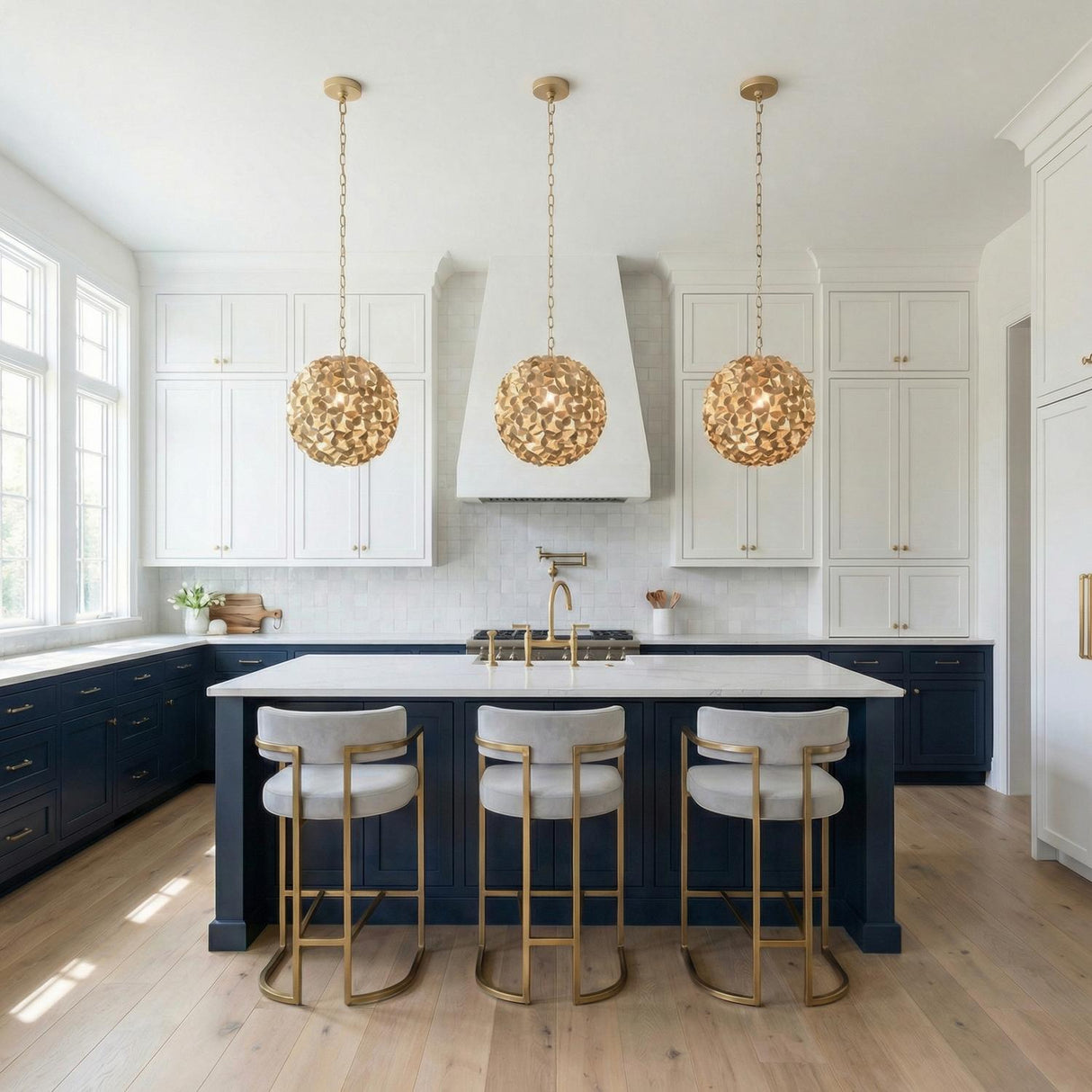 A transitional kitchen featuring three Florence Pendant 13", Soft Brass pendants over a white marble island with navy cabinets and gold-framed bar stools.