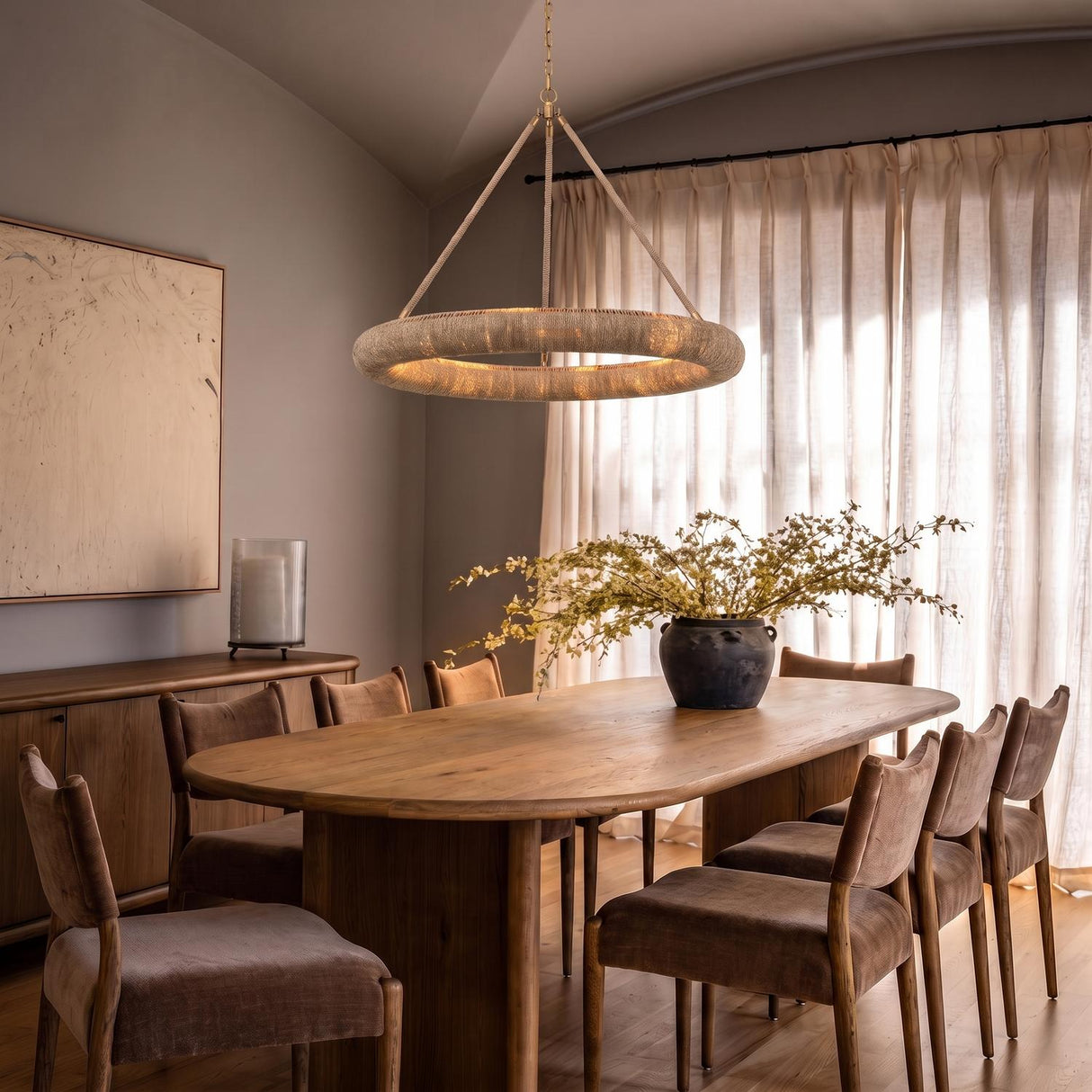 A transitional dining room with the Seabrook LED Chandelier in lake grass and soft brass over an oval wood table under a sloped ceiling with sheer curtains.