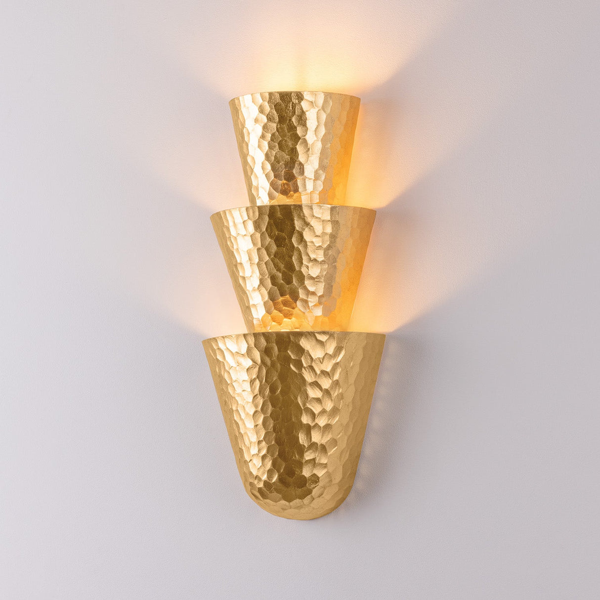 Gold wall sconce with a hammered finish on a light gray background