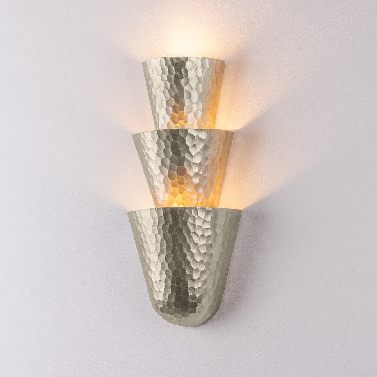 Hammered metal wall sconce with warm glow on a light gray background