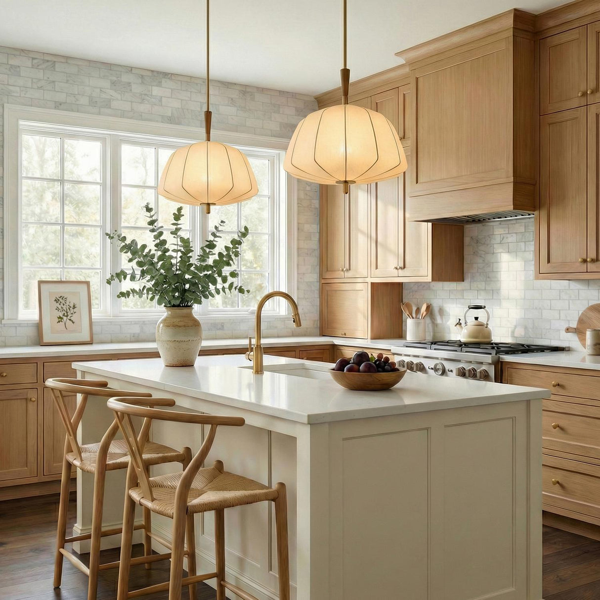 A transitional kitchen features two Winthrop Fabric Pendant, Medium, 20", Patina Brass and Wood fixtures over a white marble island with wood cabinetry and tile backsplash.
