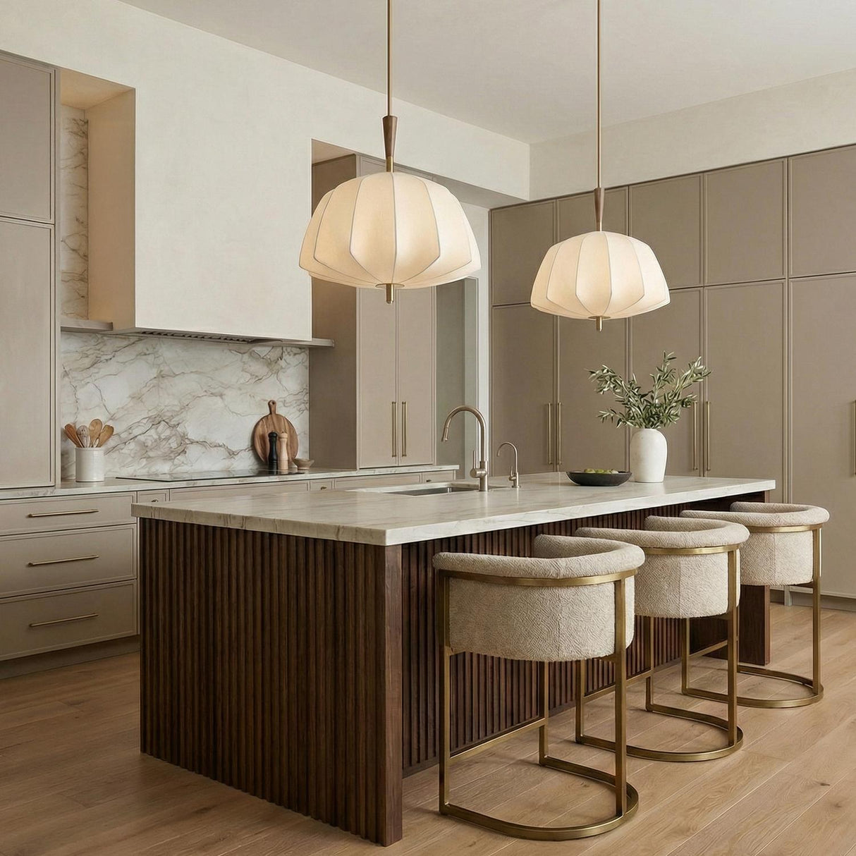 A contemporary kitchen features two Winthrop Fabric Pendant, Medium, 20", Patina Brass and Wood fixtures with linen shades over a fluted wood island and marble backsplash.