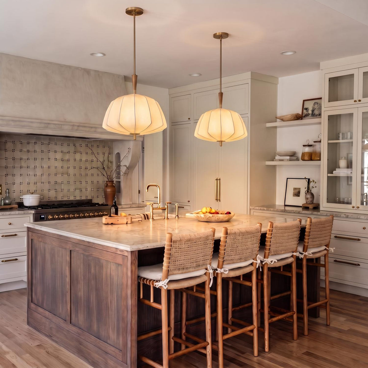 A transitional kitchen with two Winthrop Fabric Pendants in patina brass and wood over a marble island with woven bar stools and a patterned tile backsplash.