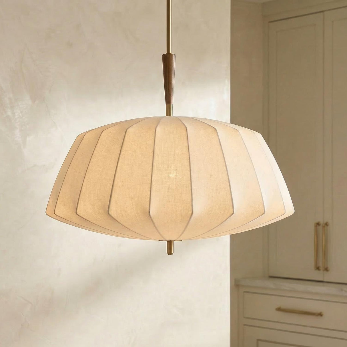 A transitional kitchen features the Winthrop Fabric Pendant, Large 32", Patina Brass and Wood with a linen shade hanging along the ceiling near beige cabinetry and marble counters.