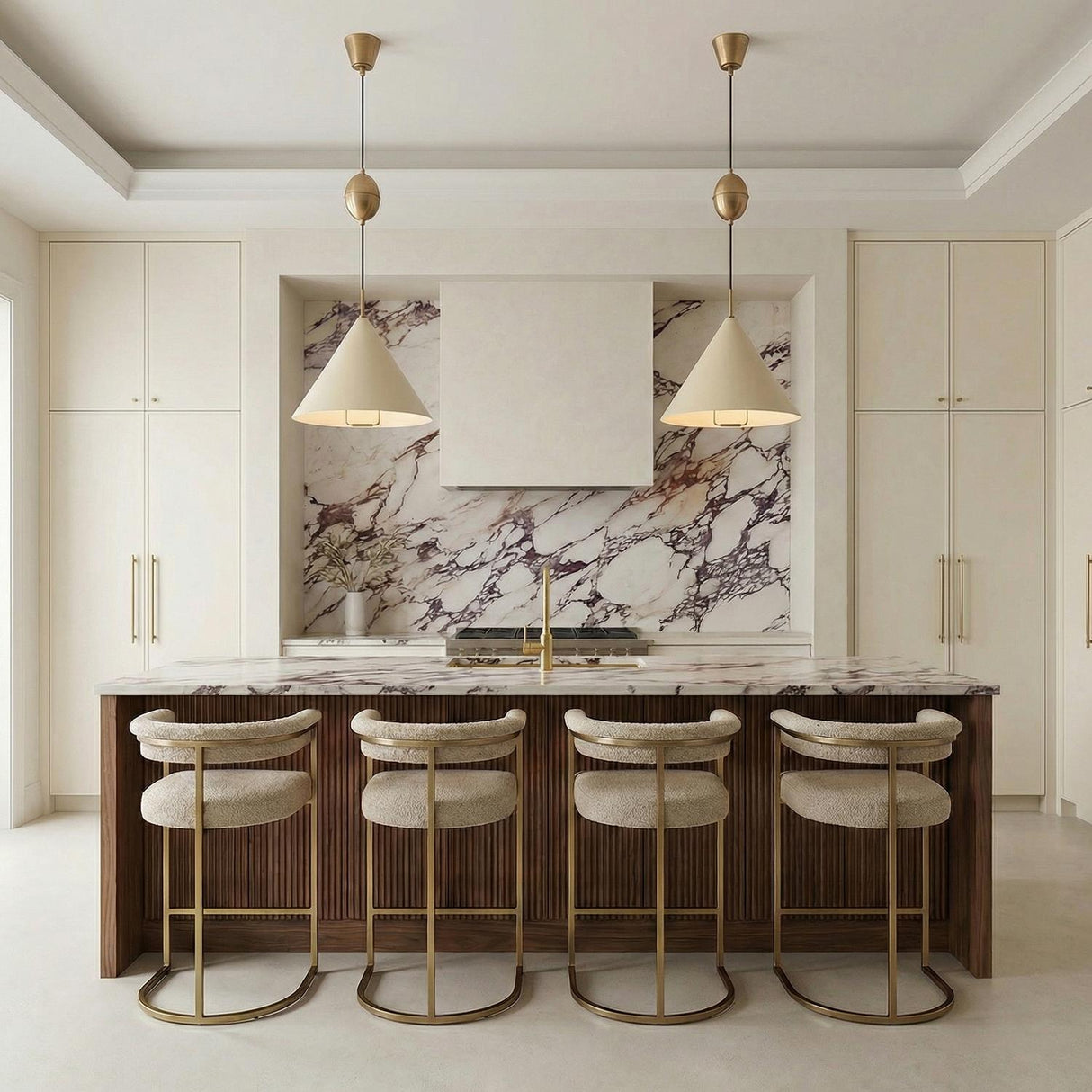 A contemporary kitchen features two Hadley Pull-Down Pendant 18", Soft Sand and Patina Brass fixtures over a marble island with wood fluting and four beige barstools.
