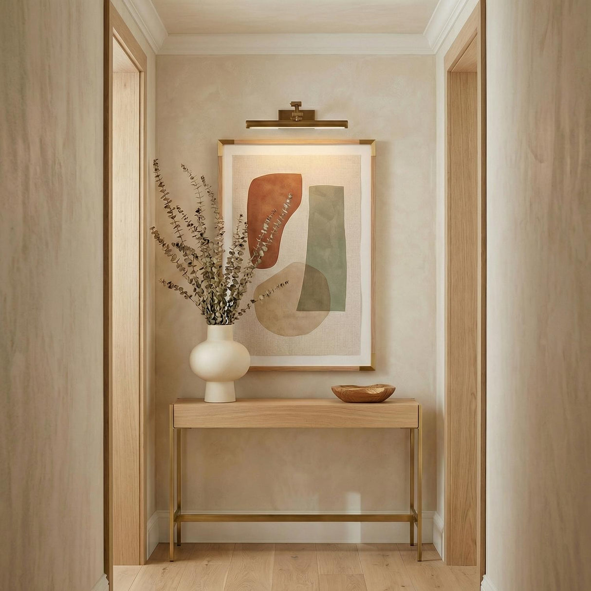 Roland LED Picture Light 16", Patina Brass linear wall sconce in a Contemporary Hallway with a light wood console and abstract art.