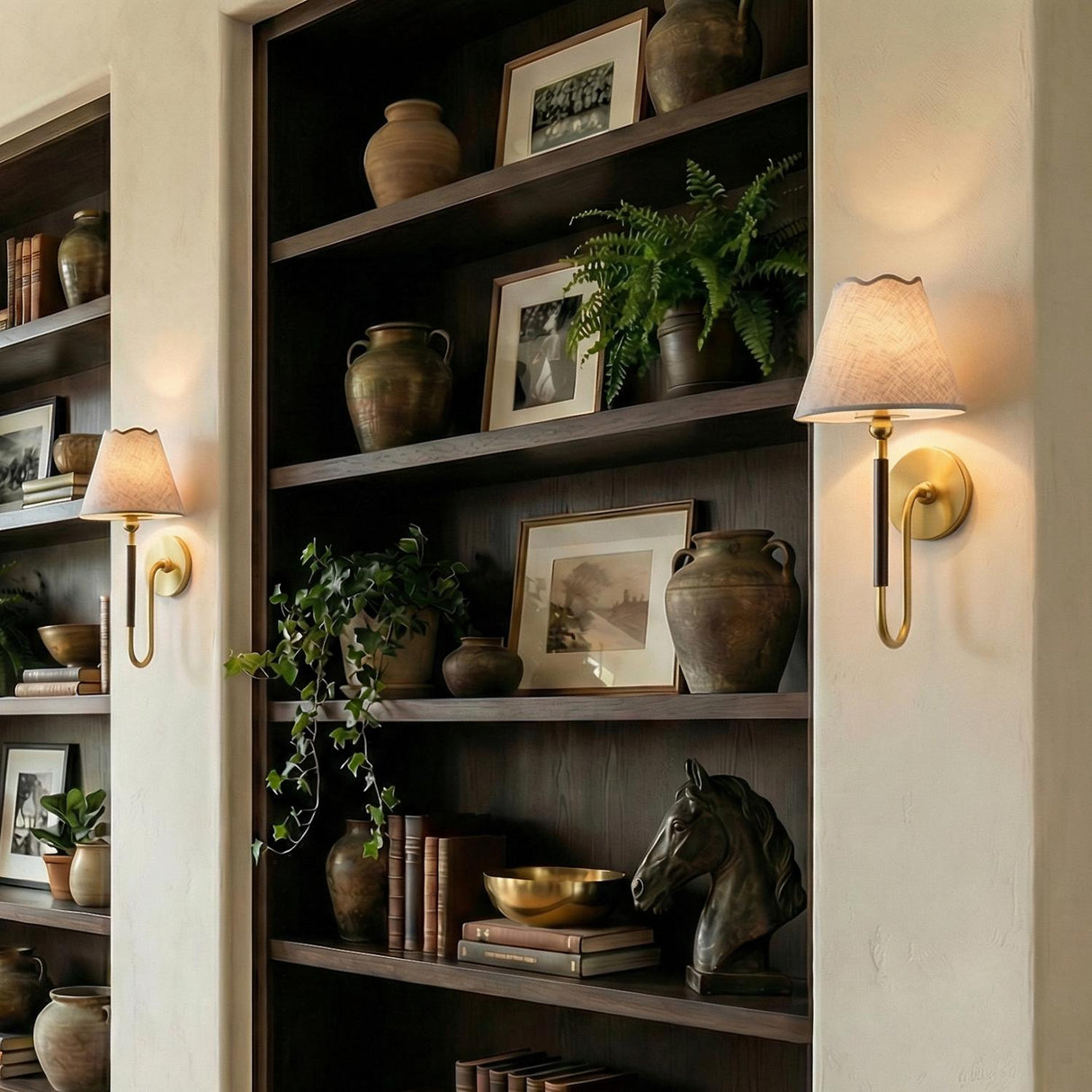 Sara Wall Sconce 17", Aged Brass and Bronze scalloped Wall Sconce in a Mediterranean Living Room with dark wood bookshelves.