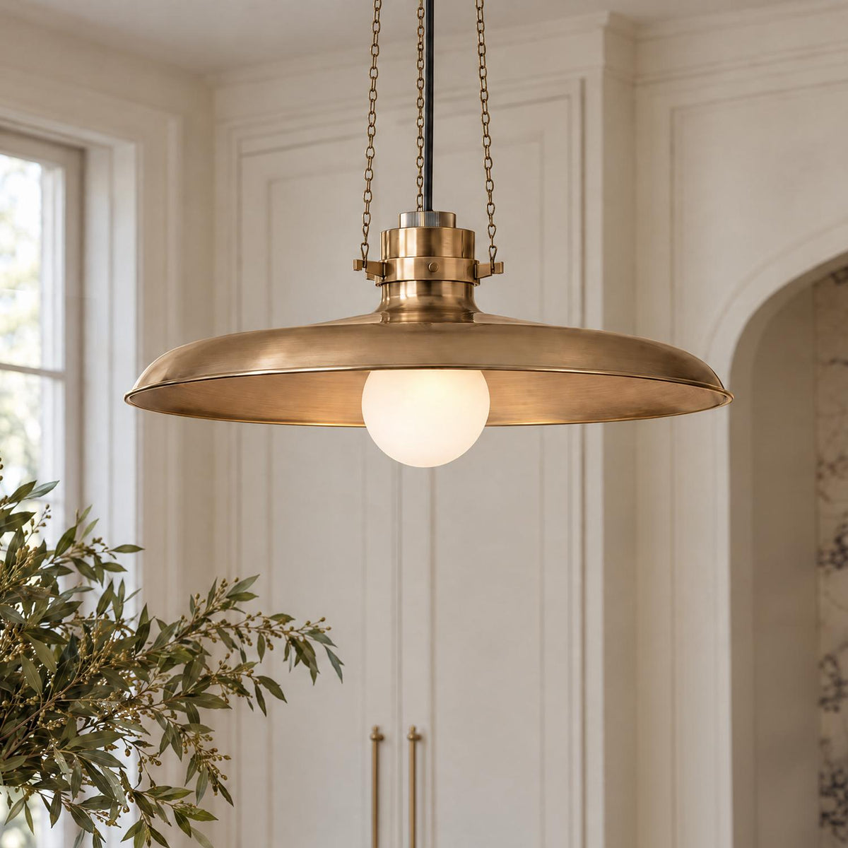 A transitional kitchen features the Titan Large Pendant 24", Patina Brass with a frosted glass globe, suspended near off-white paneled cabinetry and brass door hardware.