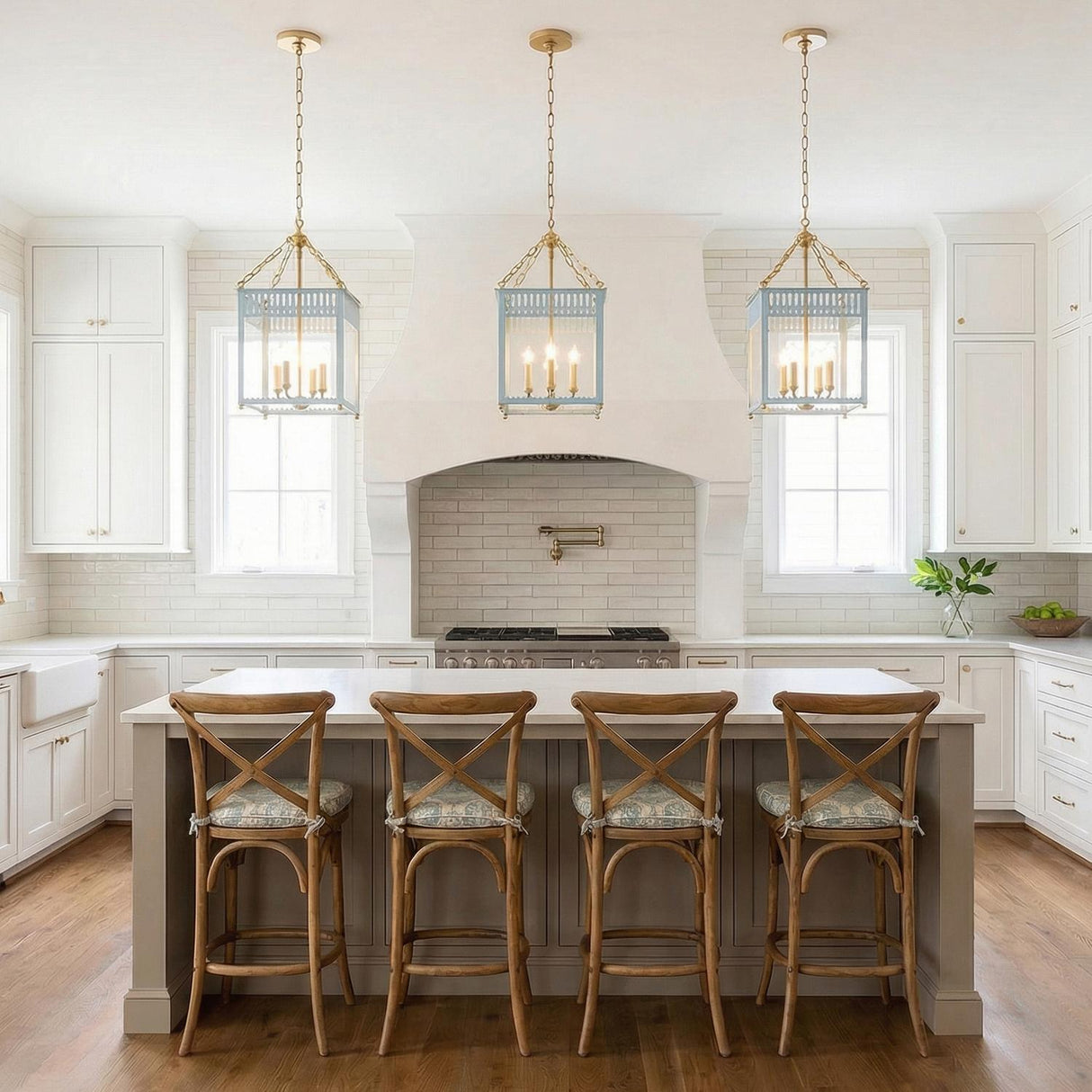A transitional kitchen with three Roanne Medium Lantern Pendant 13", Light Blue and Aged Brass fixtures over the white island with wooden cross-back barstools and subway tile.