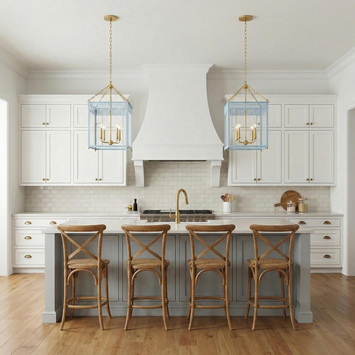 A transitional kitchen features two Roanne Large Lantern Pendants in light blue and aged brass over a gray island with white cabinets and four wood stools.
