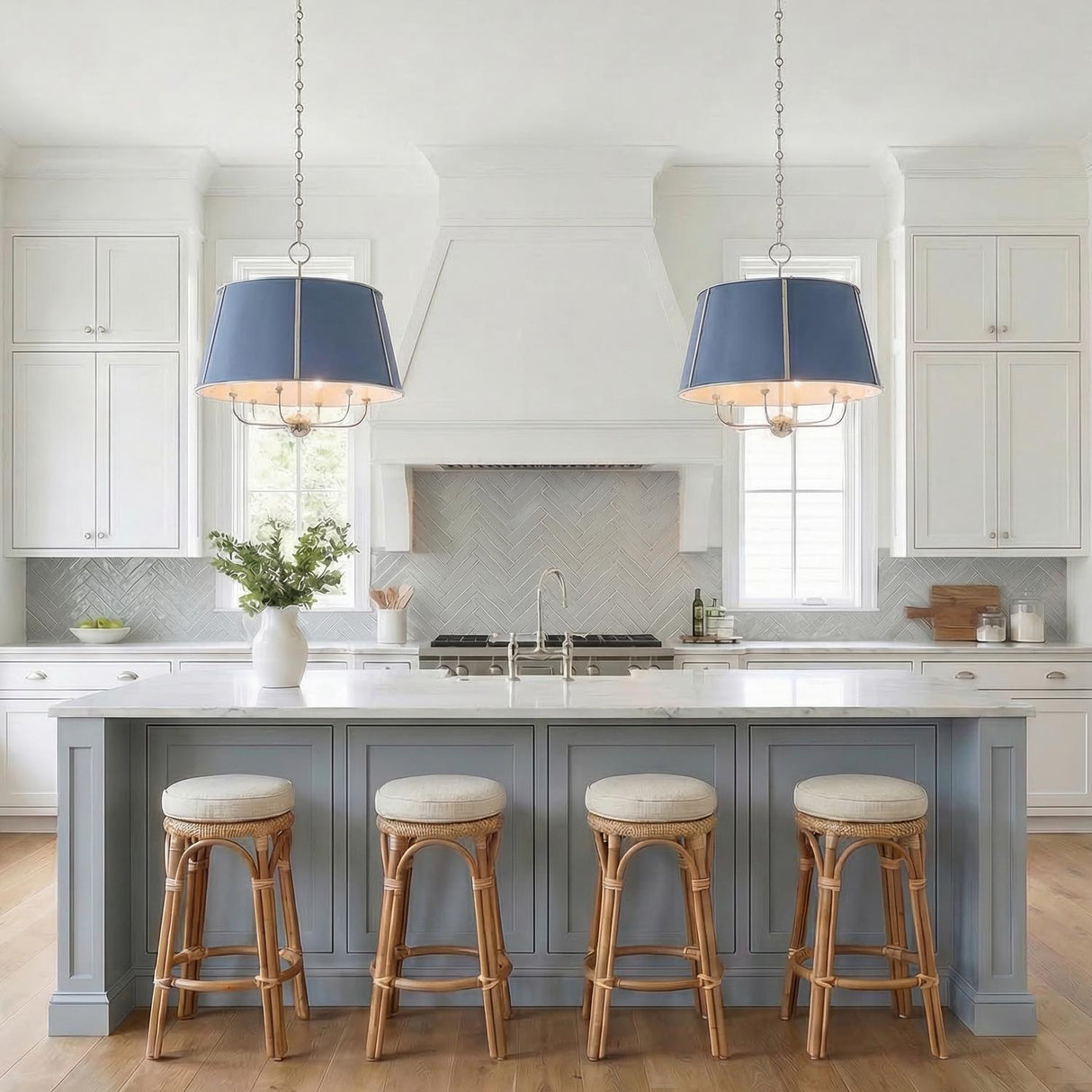 A transitional kitchen features two Avery 6 Light Extra Large Pendants in Dutch Blue and polished nickel over a marble island with rattan stools and gray herringbone backsplash.