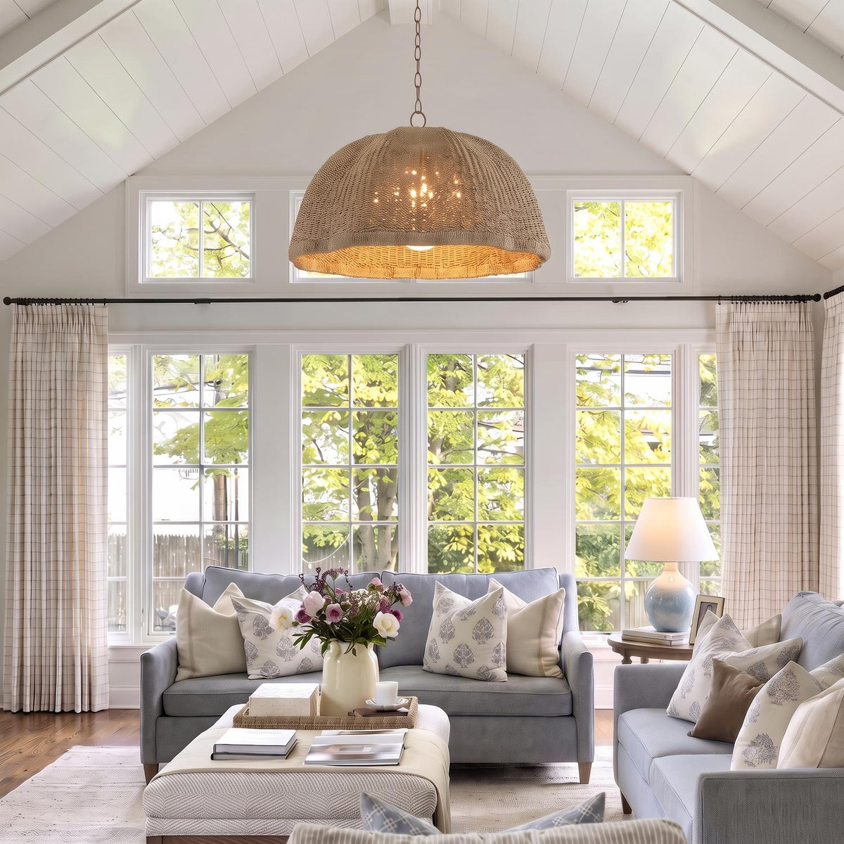 A coastal living room with a Santiago Extra Large Pendant in natural rattan and patina brass hanging from a vaulted shiplap ceiling above soft blue sofas.