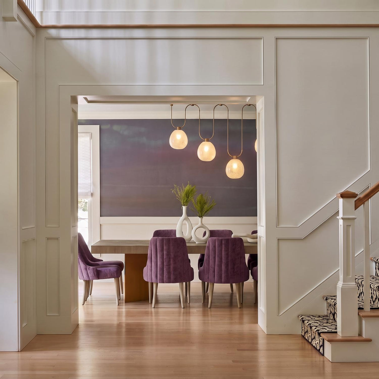 A transitional dining room with the Orly 4 Light Linear Chandelier in patina brass and seeded cloud glass under a double-height ceiling with purple chairs.