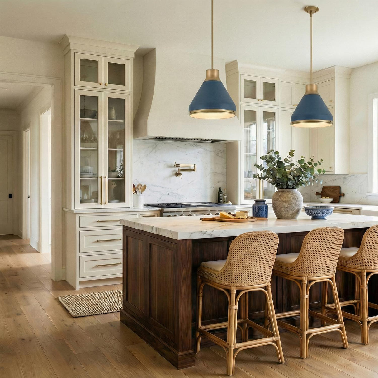 A transitional kitchen features two Drew Medium Pendant 19" Vintage Blue and Aged Brass fixtures over a marble island with dark wood cabinets and woven rattan stools.