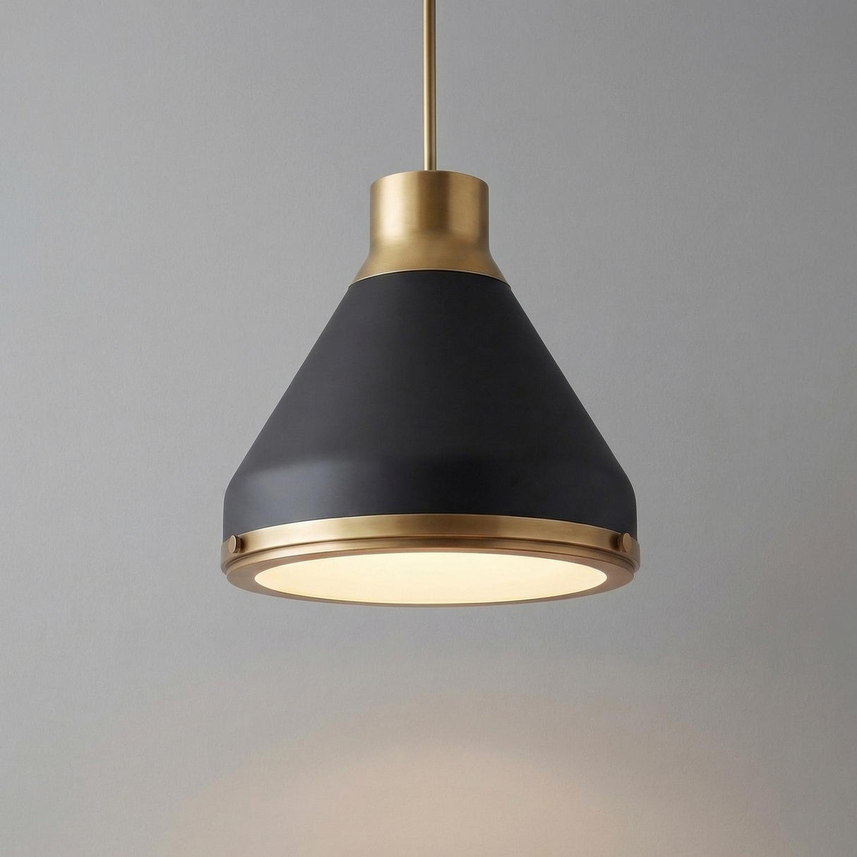A modern kitchen features the Drew Medium Pendant 19", Matte Black and Aged Brass hanging over an island against a simple gray wall with a frosted glass diffuser.