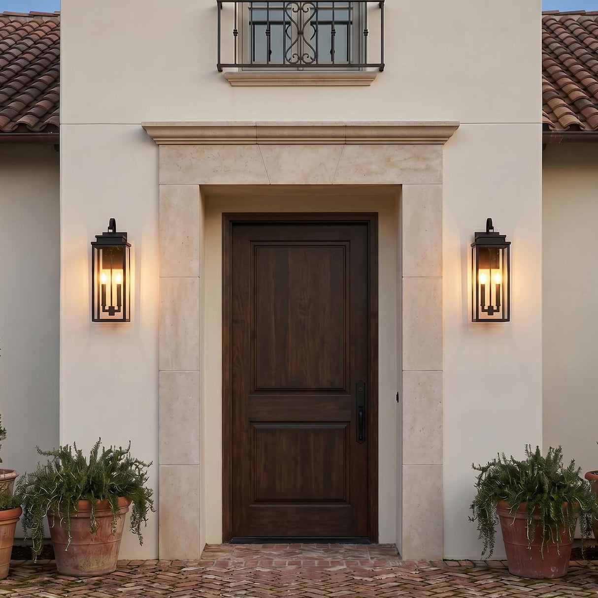 A Mediterranean entryway featuring two matte black Trevor Outdoor Wall Light lanterns flanking a dark wood front door set within a stone surround and brick pathway.
