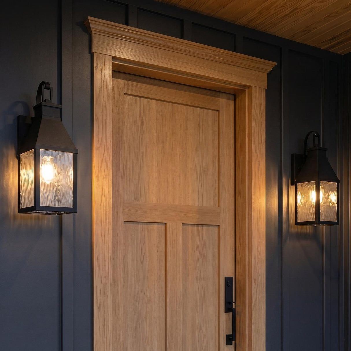 A craftsman porch entry featuring two matte black Westin Outdoor Wall Light lanterns with water glass flanking a light oak door on dark board-and-batten siding at twilight.