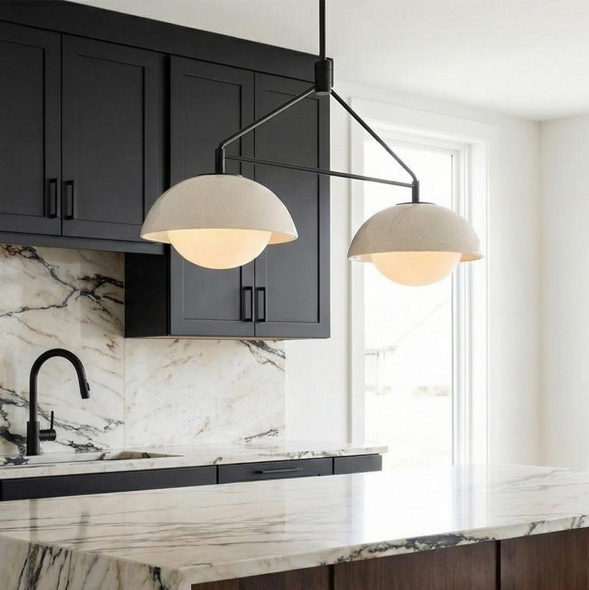 A kitchen features the Hanley 2 Light Linear Pendant 32", matte black and ivory crackle ceramic over a marble island with black cabinets and a marble backsplash.