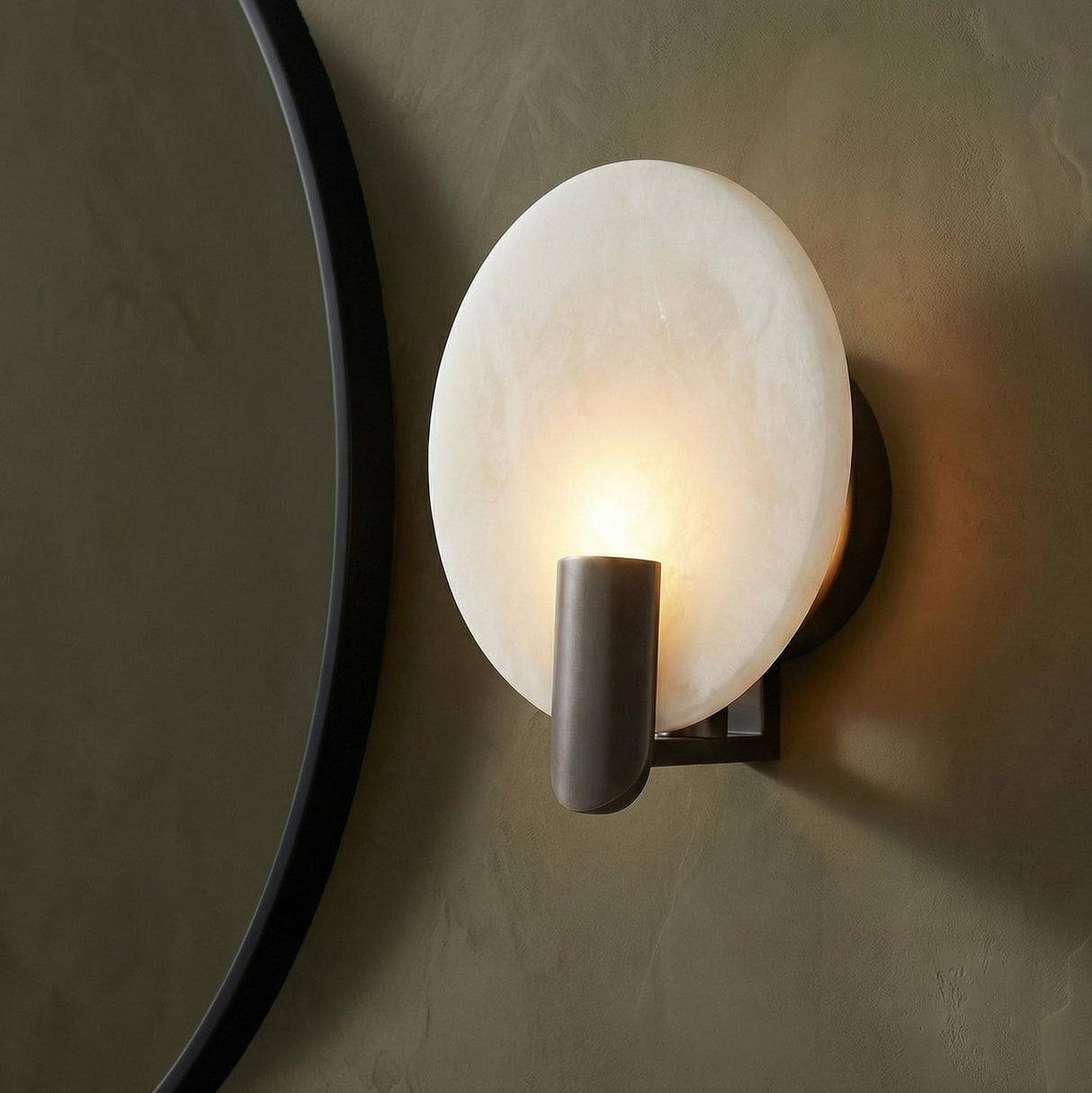 Othello Wall Sconce 9", Bronze and Onyx geometric Wall Sconce in a Contemporary Bathroom with a black circular mirror and olive wall.