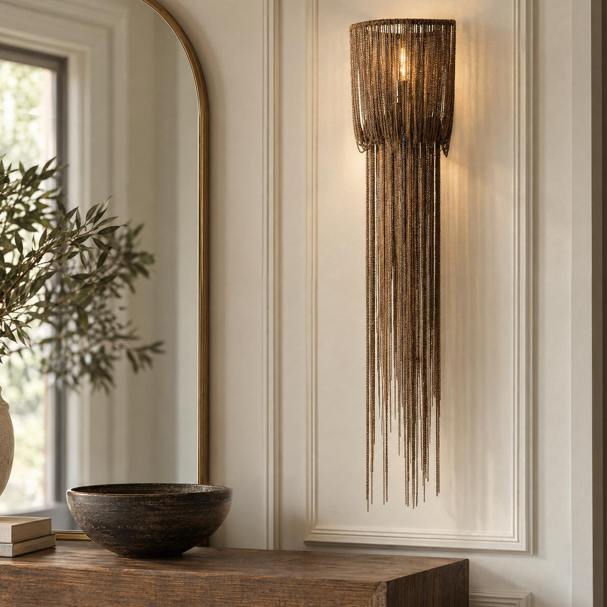 A transitional foyer features the Talon Extra Large Wall Sconce in antique burnished brass mounted on wall paneling beside an arched mirror and dark wood console table.