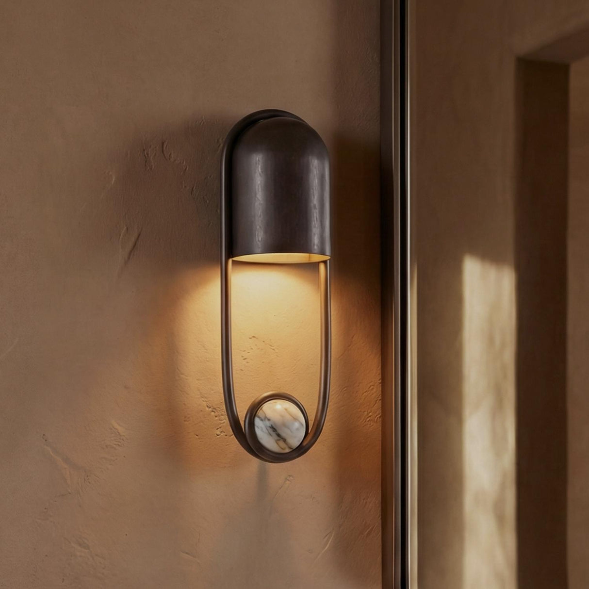 A contemporary hallway with a Bastion Wall Sconce 15", English Bronze with Marble Accent mounted on a textured plaster wall next to a dark doorway.