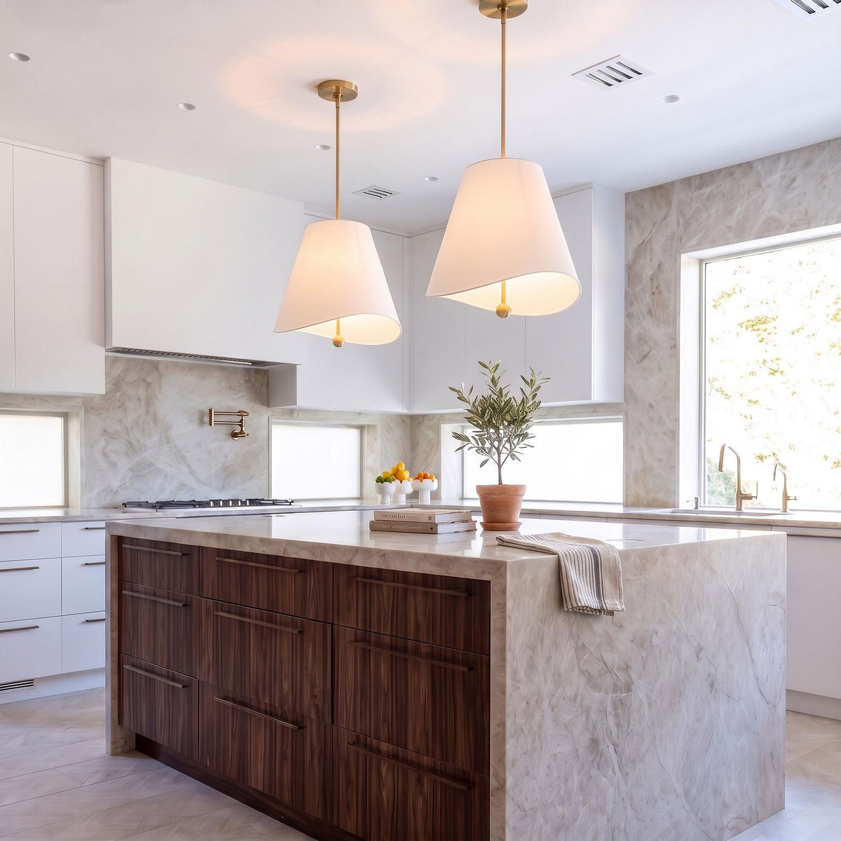 A modern kitchen with two Jada Large Conical Pendants in Modern Brass with white shades over a marble waterfall island and dark wood cabinets.