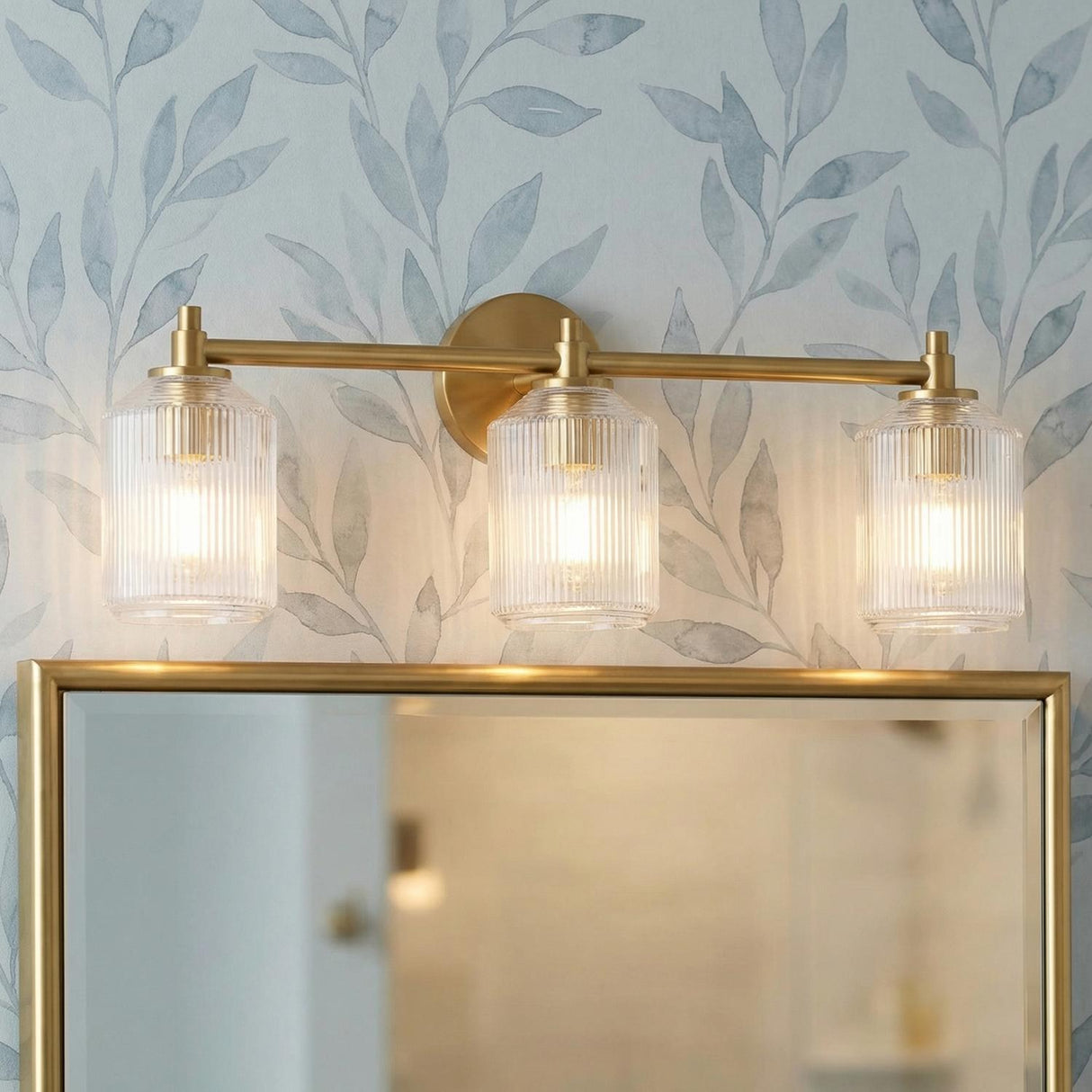 Lathan 3 Light Vanity 26", Modern Brass linear glass Vanity in a Transitional Bathroom with leaf wallpaper and a gold mirror.