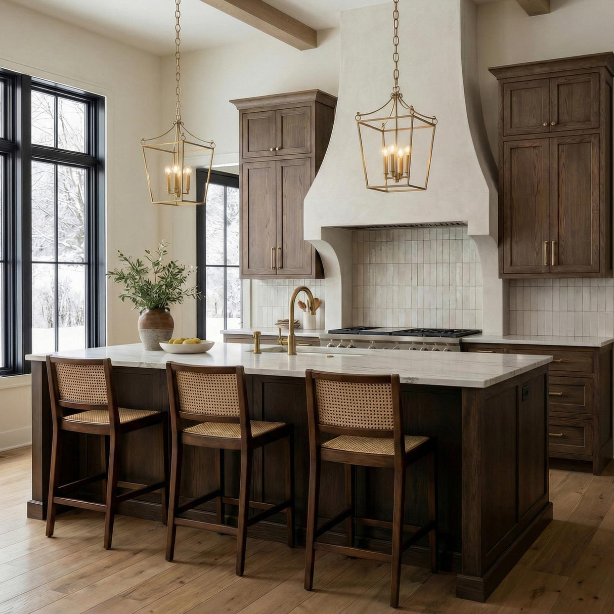 A transitional kitchen features two Cambria Small Lantern Pendant 14", Modern Brass fixtures over a white marble island with dark wood cabinets and a beamed ceiling.