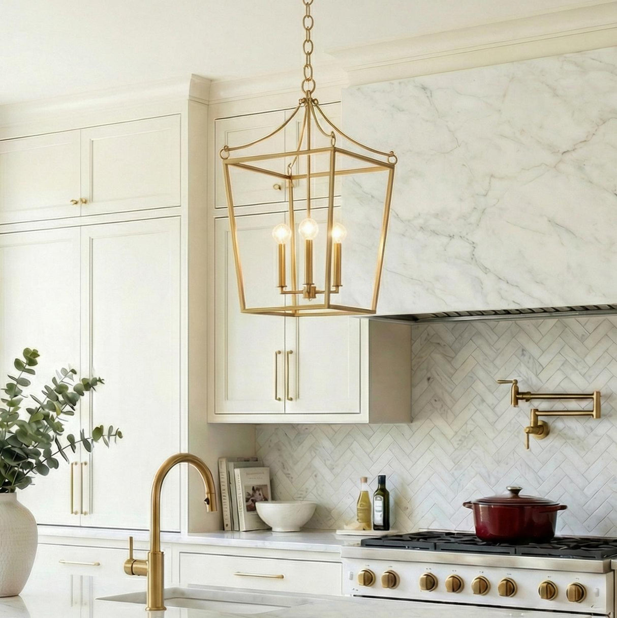 A transitional kitchen features the Cambria Large Lantern Pendant 21", Modern Brass over a white marble island sink with white shaker cabinets and a marble herringbone backsplash.