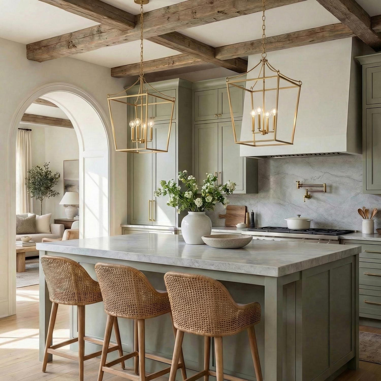 A transitional kitchen features two Cambria Extra Large Lantern Pendant 24", Modern Brass fixtures over a marble island with sage cabinets and barstools under a beamed ceiling.