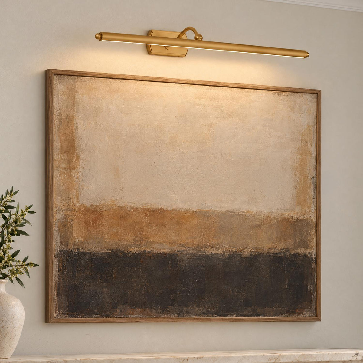 A modern living room features the Bria LED Picture Light 24", Modern Brass mounted above framed abstract artwork with a textured ceramic vase.
