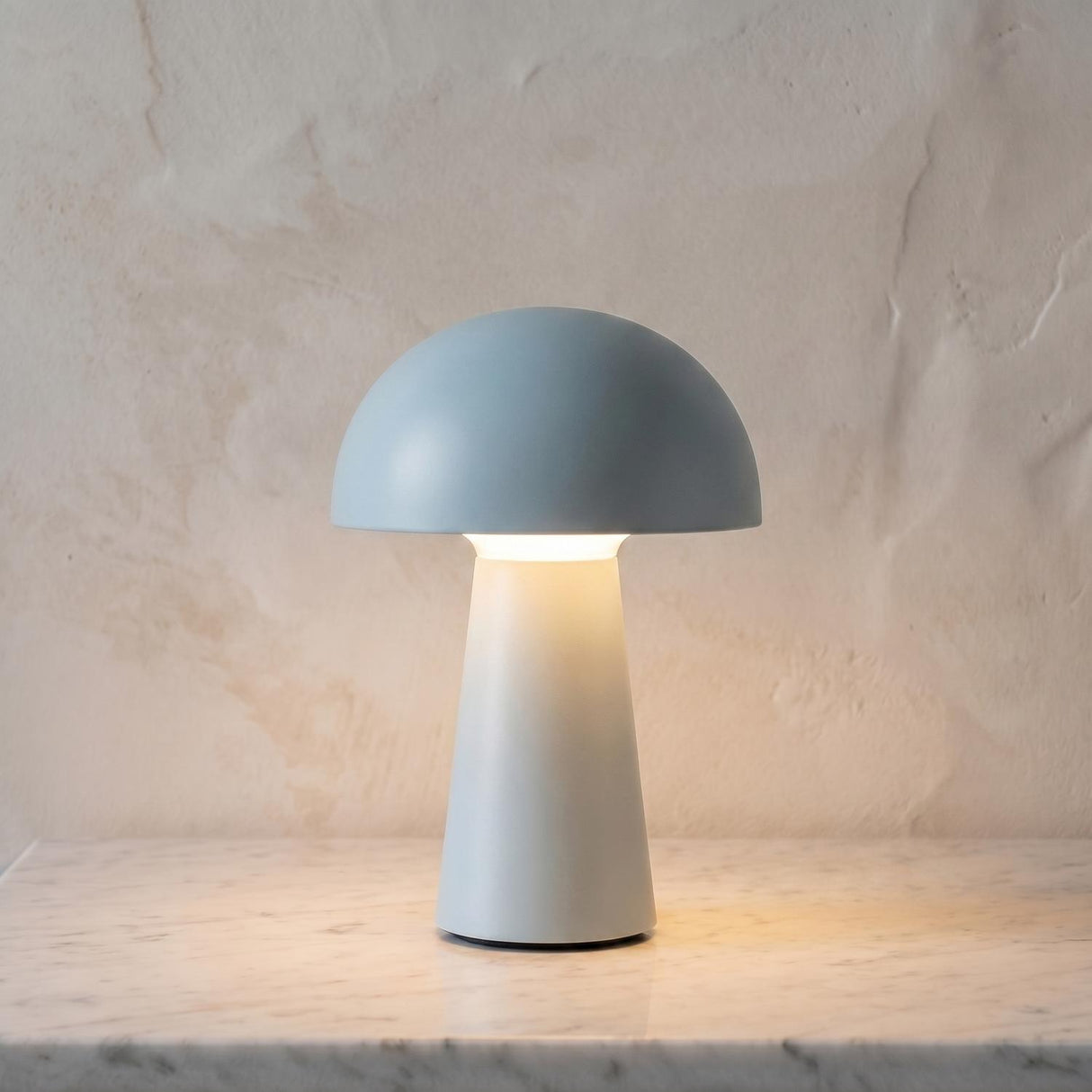 A modern living room with a baby blue matte finish table lamp on a white marble countertop set against a neutral textured plaster wall backdrop.